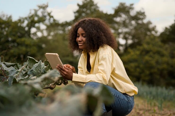 A smiling farmer reading a tablet among kale plants