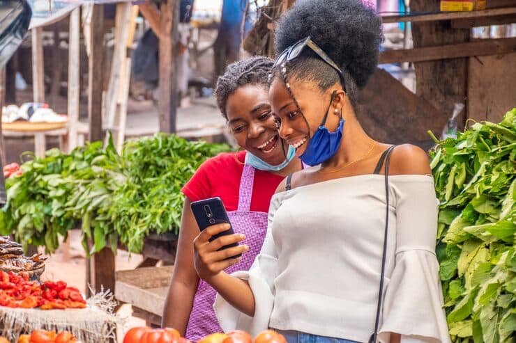Two women laughing at a phone at a local market stall