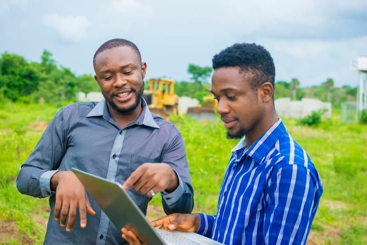 Two men looking at a laptop together on farmland