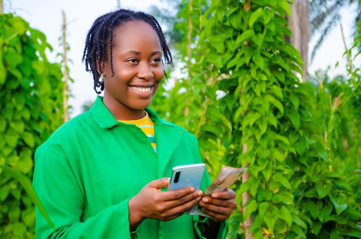 A smiling farmer holding a phone and cash in a bean field